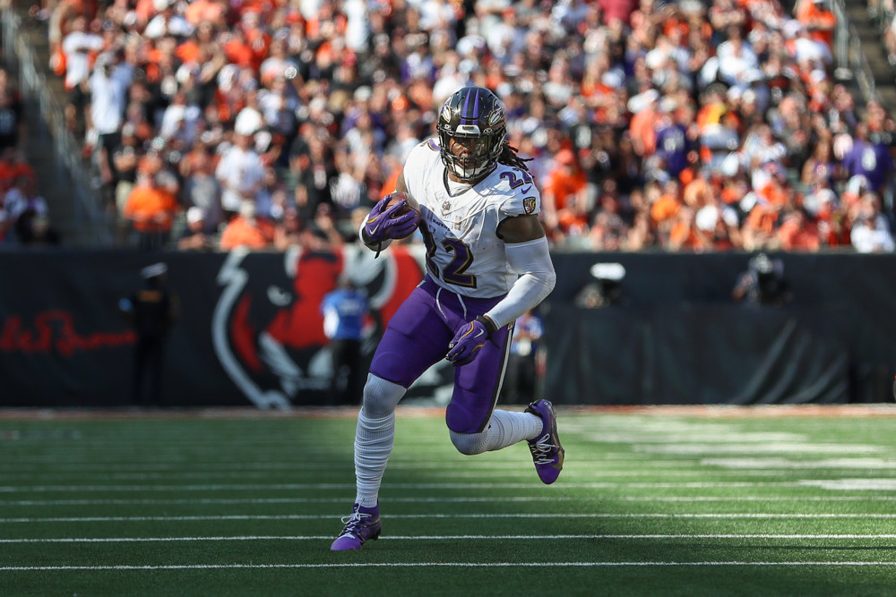 Derrick Henry, in white shirt and purple pants, runs upfield for the Ravens with the ball tucked under his right shoulder